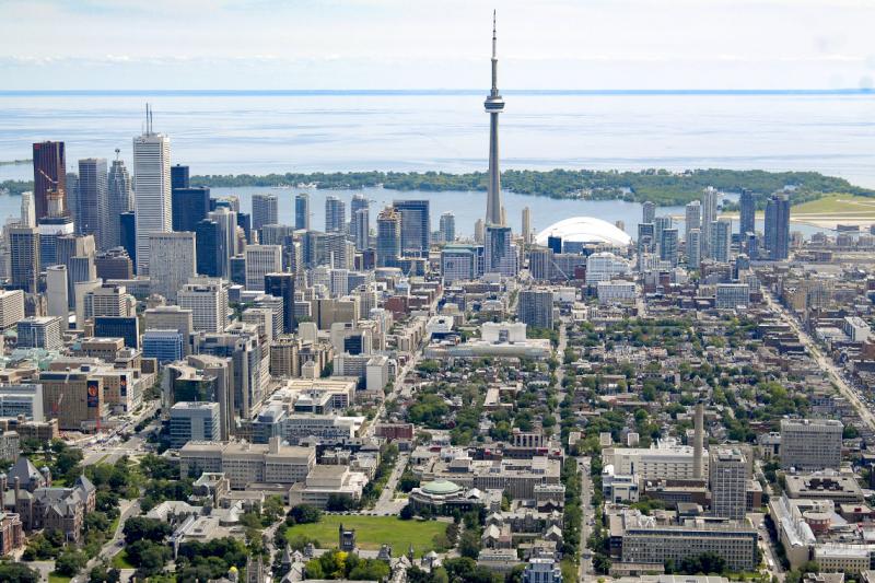 The view from an airplane of the leafy U of T campus next to downtown Toronto's office buildings and a calm Lake Ontario.