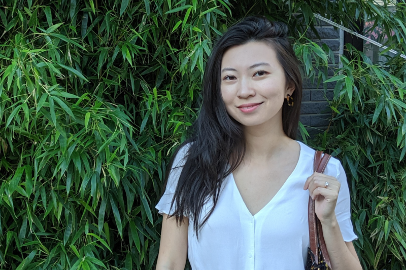 Lulu Li smiling and standing in front of a bamboo hedge.