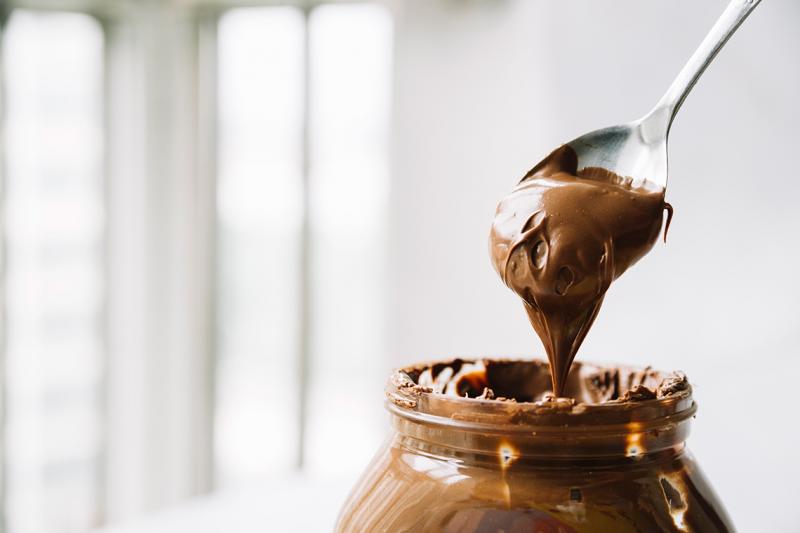 Picture of a messy jar of hazelnut chocolate spread, with a spoon lifting out a large scoop.