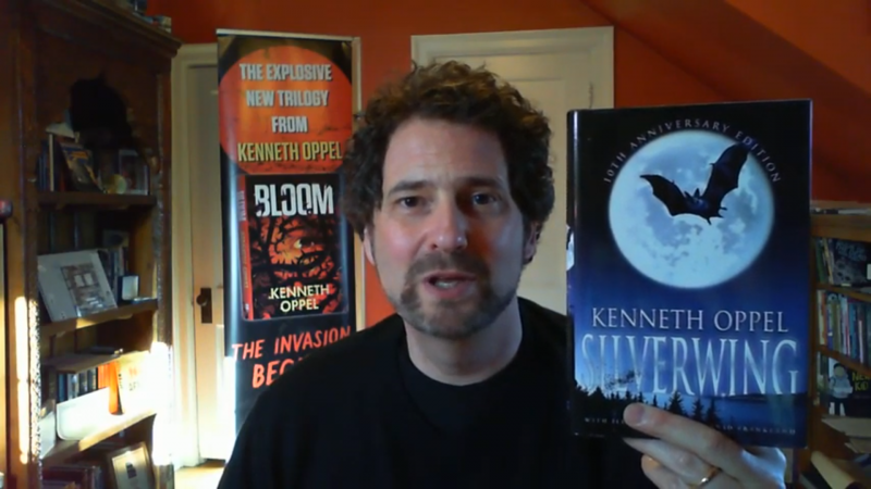 Kenneth Oppel smiles and holds up his book Silverwing in this still from a video.