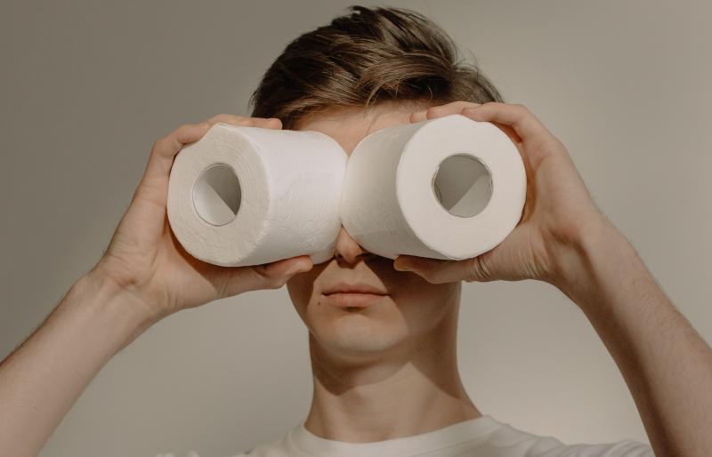 A young man holds rolls of toilet paper up to his eyes as if they were binoculars.