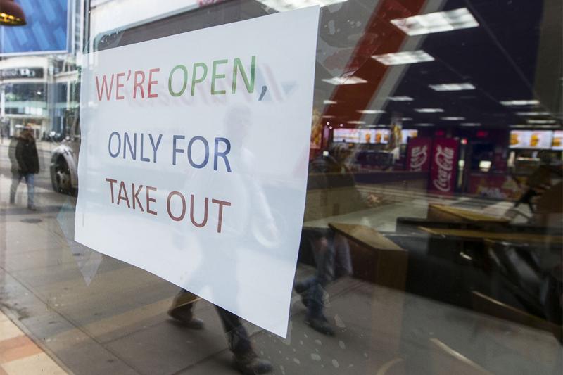 A sign in a restaurant window reads: We're open, only for take-out. 