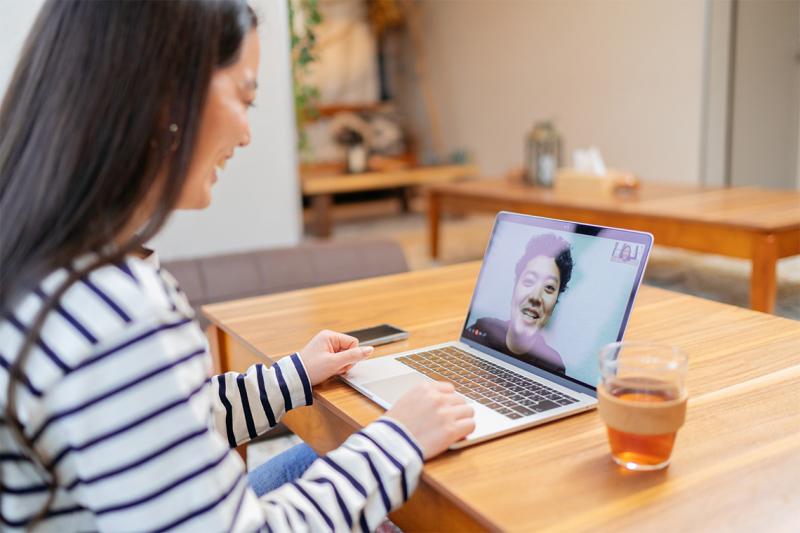 Two women laugh as they talk in a video call, one sitting looking at a laptop screen and the other on the screen itself.