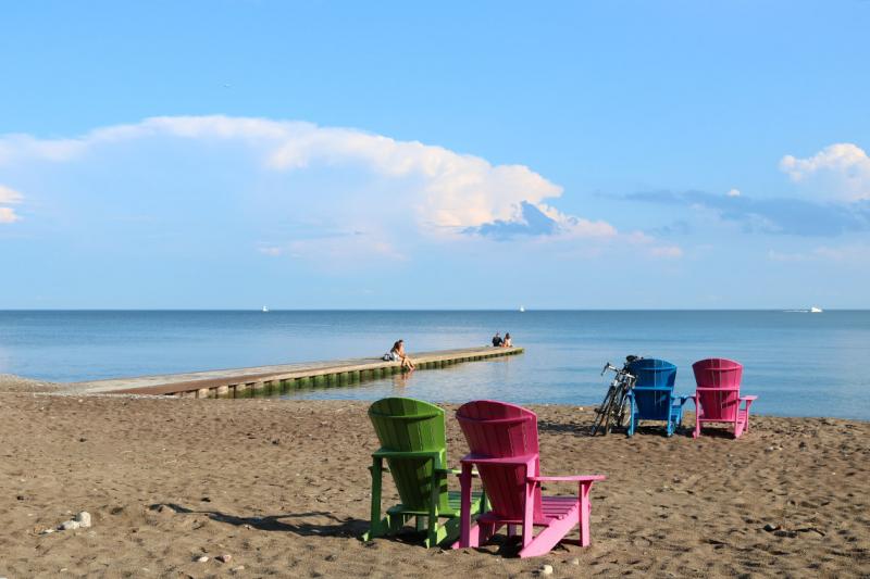 Empty Muskoka chairs sit in pairs on a sunny, deserted beach.