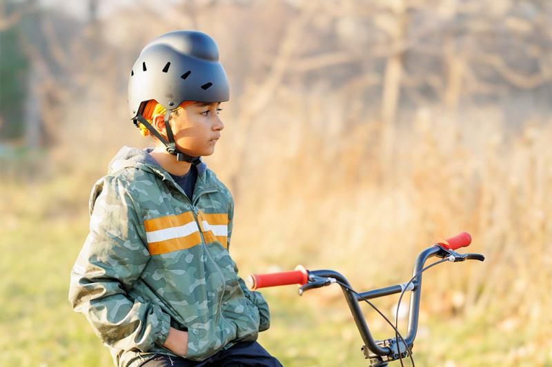 A boy stands beside his bike wearing a helmet that allows for his headcovering
