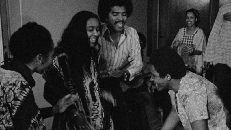 A film still from OYOYO (1980) showing a group of people smiling and clapping.