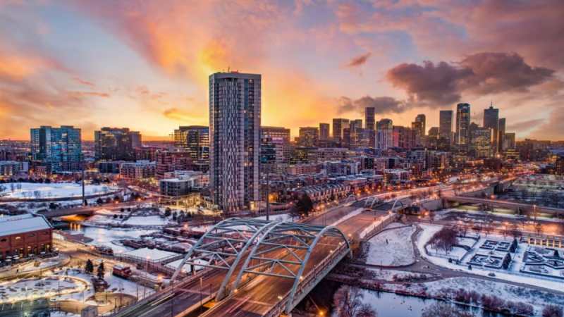 Image of a sunset, with a skyscraper and a bridge with snow on the ground.