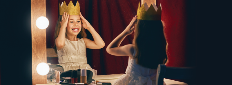 Little girl staring in the mirror putting on a crown