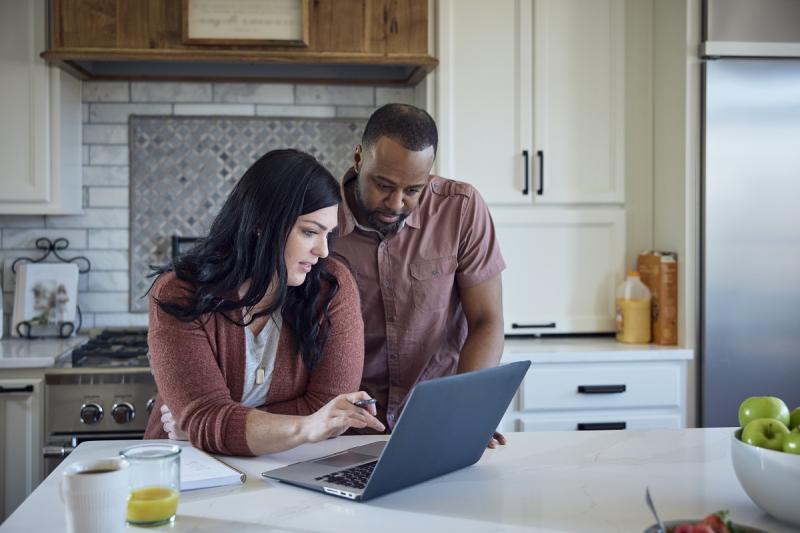 Couple reviews laptop screen together in a home setting.