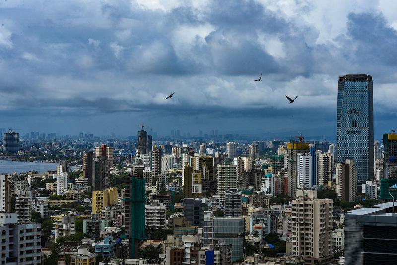 Cityscape of Mumbai, India with high-rise buildings and birds flying in the sky.