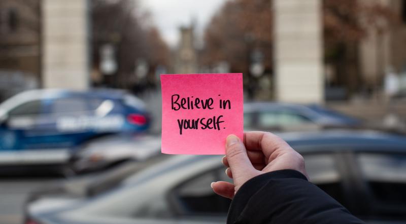 Person holding sticky note that says "Believe in Yourself.