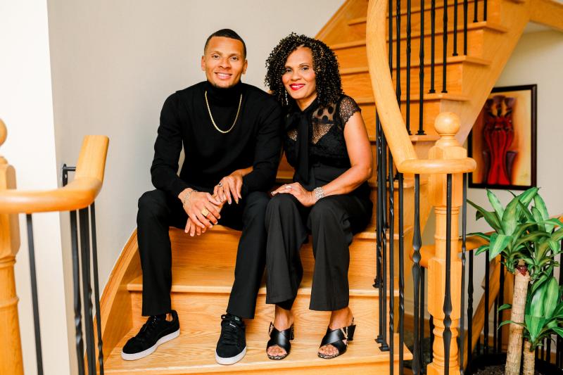Andre De Grasse, his mother Beverley De Grasse, black male and female, shown smiling and sitting on stairs.