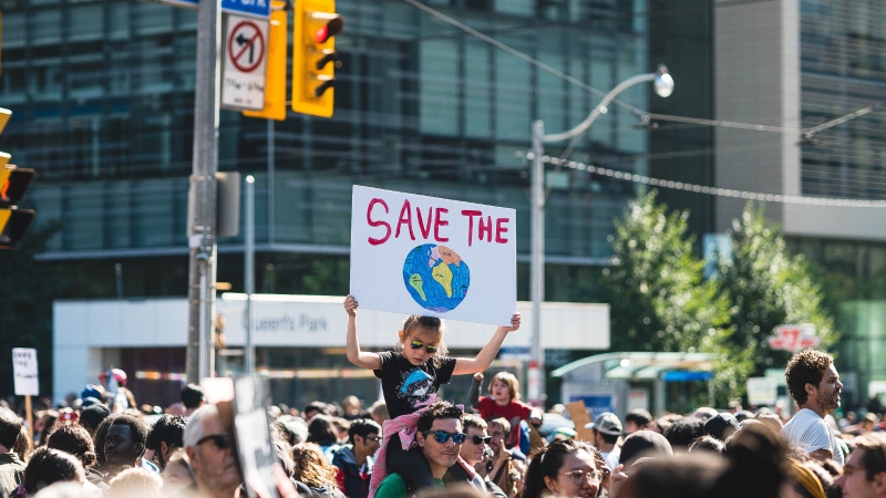 Child on parent's shoulder with poster which says Save the Planet.