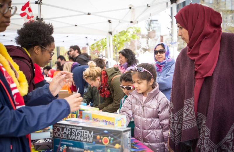 Image shows families visiting science exhibitions staffed by student volunteers.