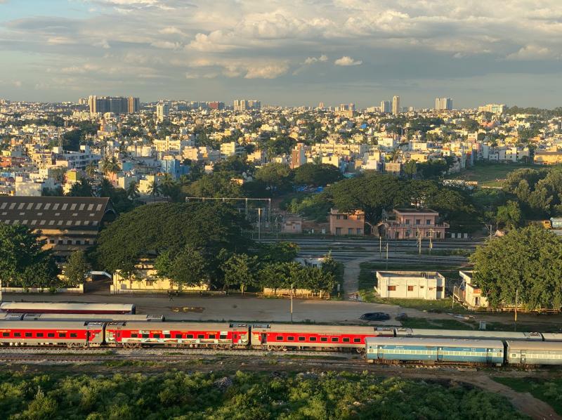 Bengaluru skyline. Trains in front, foliage in middle distance, buildings in far distance.