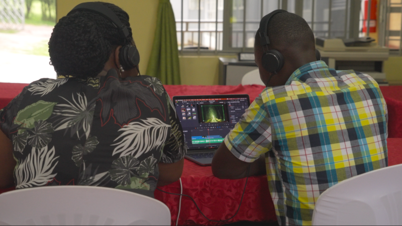 Two men wearing earphones edit a video on a laptop