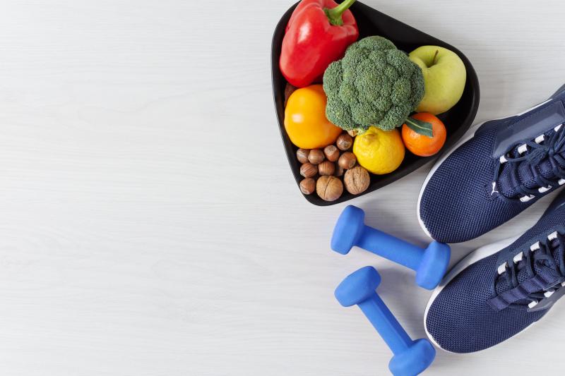 Image of navy sport shoes, blue light weights and a bowl of fruits and vegetables.