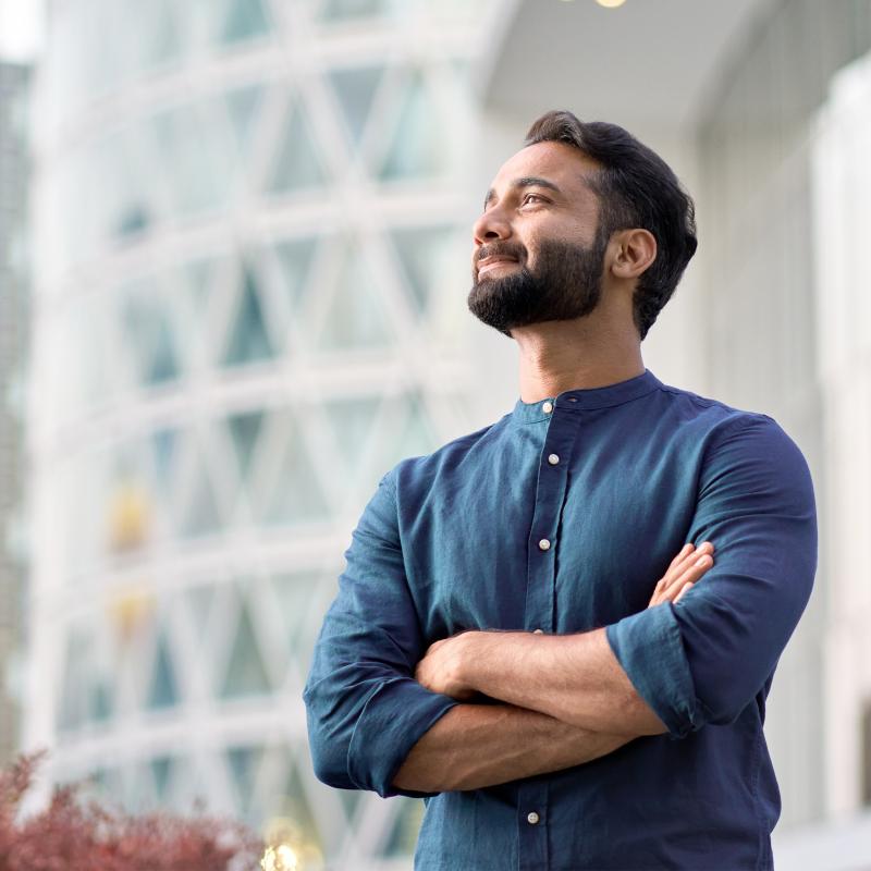 Confident Indian man standing in modern big city looking afar.