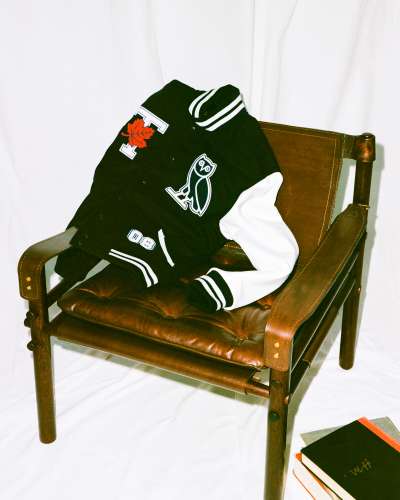 A jacket with the U of T letter T and maple leaf logo next to the OVO owl logo, draped over a chair near books.
