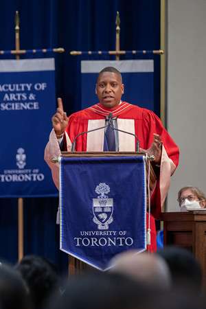Masai Ujiri gestures while speaking in Convocation Hall, wearing academic robes.