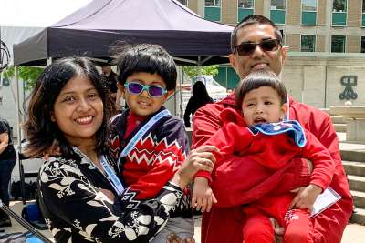 Biplob Mazumdar smiles happily with his wife and two young boys, outdoors on St. George Street.