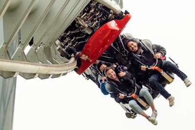 People scream happily on an amusement park ride where they dangle beneath a rollercoaster track.