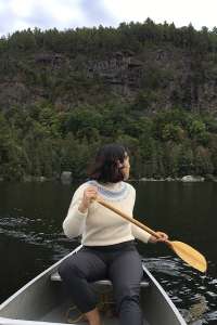 Alexandra Gaspar looks over her shoulder as she steers a canoe on a calm lake.