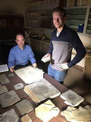 Jean-Bernard Caron and Joe Moysiuk stand in front of a table covered in flat rocks, each showing the imprint of a fossil.