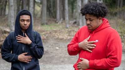 Two young Black men standing in nature with their hands on their hearts. 