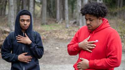 Two young Black men standing in nature with their hands on their hearts.