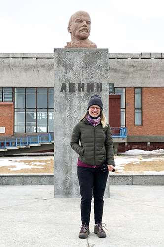 Alina Bykova smiles as she stands on snowy ground in front of a concrete bust of Lenin.