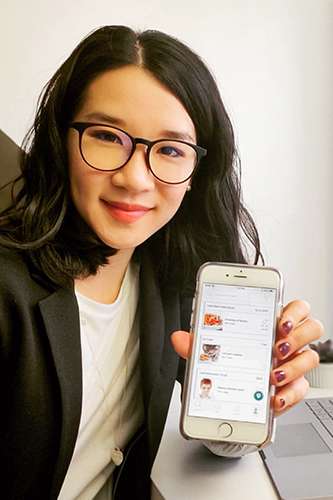 Catherine Chan smiles as she holds up her phone with Honeybee Hub displayed on the screen.