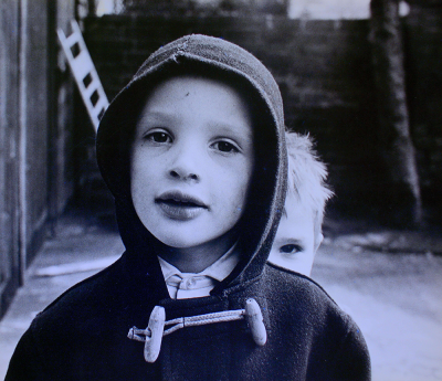 A small boy peeks from behind another boy's shoulder in an old photograph.