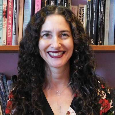 Dana Seitler smiles while sitting in front of a bookcase stuffed with books.