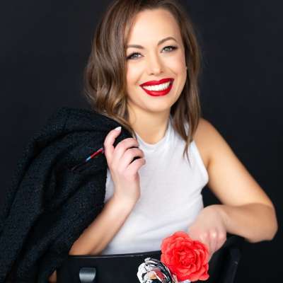 Close-up of Danielle Dinunzio wearing red lipstick and a white shirt, holding a red flower.