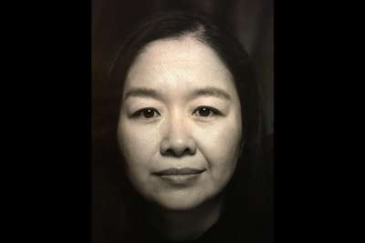 A portrait of Dawn Lim looking serious and sitting in the dark.