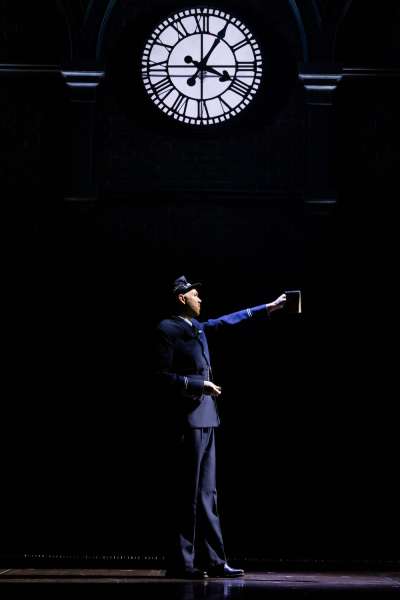 Mark Crawford in costume as an old-fashioned train conductor, standing beneath an elaborate clock.