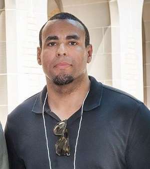 Ike Okafor stands in front of a stone archway, smiling