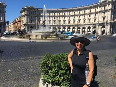 Ivana Di Millo smiles, standing in a cobbled city square with an elaborate fountain.