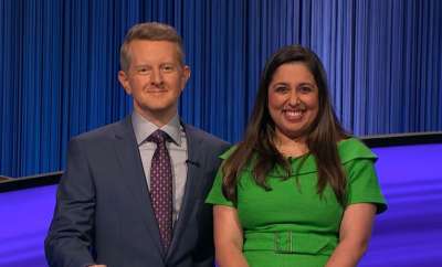 Juveria Zaheer stands smiling next to Jeopardy! host Ken Jennings on the Jeopardy set.
