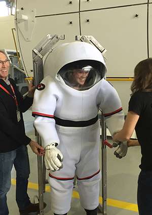Katie Harris laughs while trying on a spacesuit. The helmet is six times the size of her head.