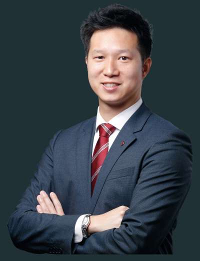 Man in gray suit with red tie standing with arms crossed.
