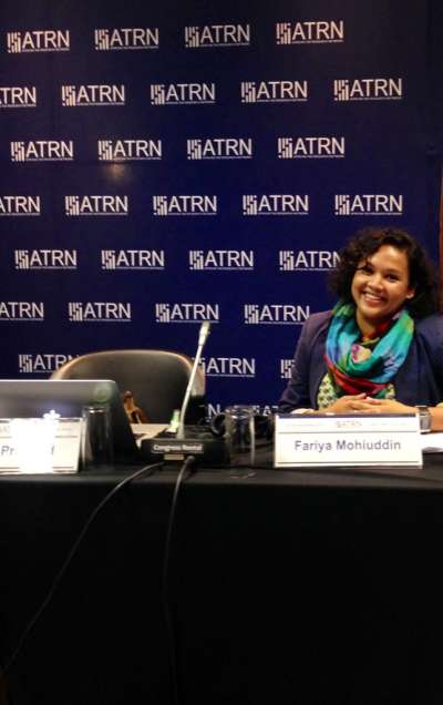 Fariya Mohiuddin smiles, sitting at a conference table behind her nameplate.