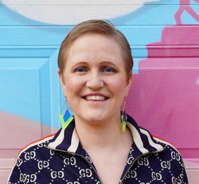 Margaret Lonieswska smiles happily while standing in front of a colourful wall mural.