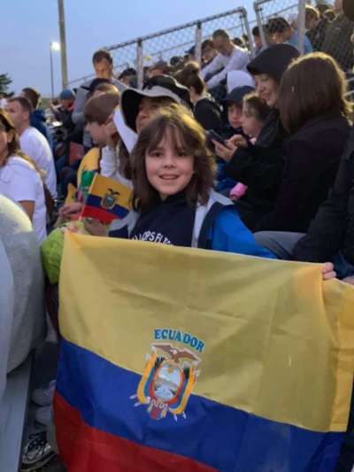 An 11-year-old Daniel Honciuc Menendez on bleachers holding an Ecuadorian flag