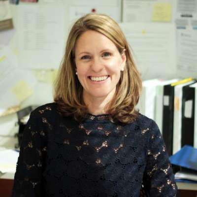 Renee Brost smiles, sitting in front of a bulletin board covered with notes.