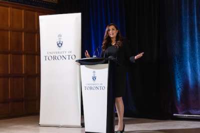 Samra Zafar gestures as she speaks at a podium. The banner beside her reads: University of Toronto.