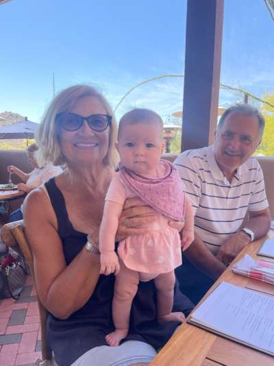 Susan Allen holding her baby granddaughter, sitting at a restaurant outdoors next to her husband.