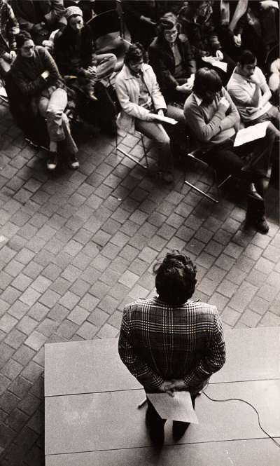 Seen from overhead, a man stands quietly on a lecture platform in front of a lecture theatre.