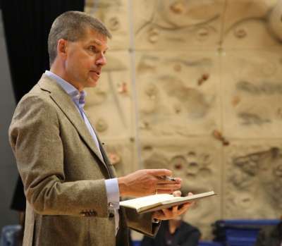 Tye Farrow gestures, holding a book, as he speaks to an audience.